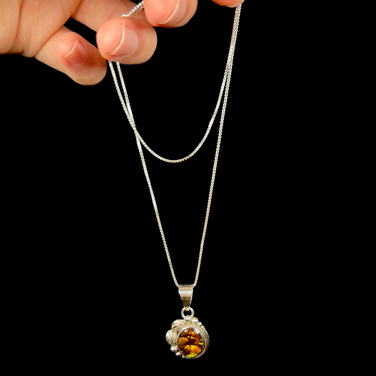 Hand dangling women's sterling silver fire agate necklace from box-style chain against black background.