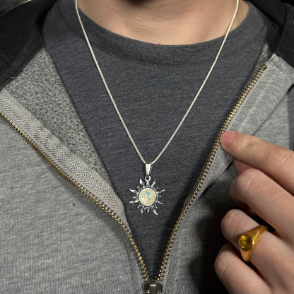 Close-up of a women's Boho-inspired sterling silver sun necklace mounted with an imitation opal worn around a person's neck against a dark shirt.