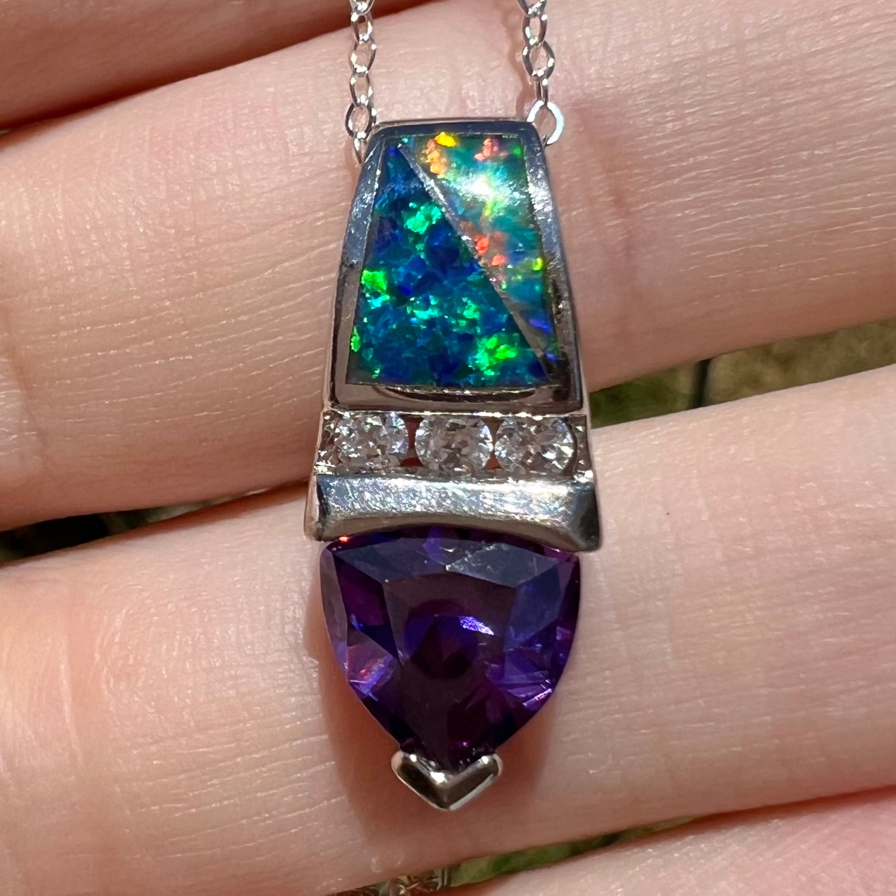 Close-up of a women's sterling silver lab-created opal inlay and purple trillion cut gemstone pendant, resting in a hand under natural sunlight.