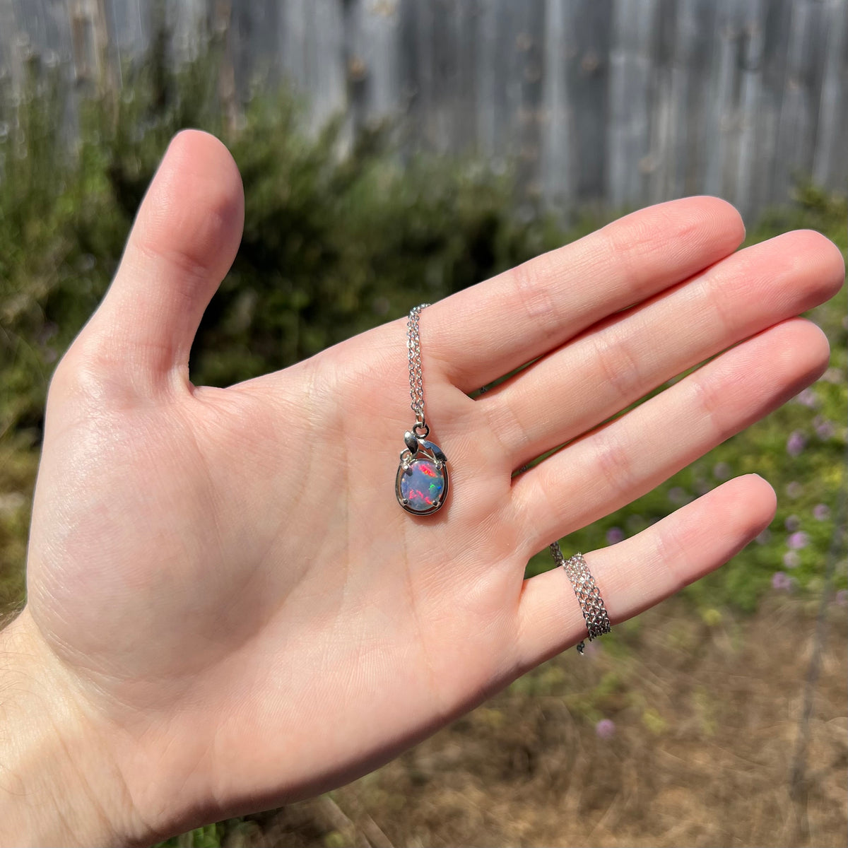 Hand holding women's triplet opal necklace in sunlight; the opal has bright red flashes of color