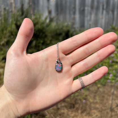 Hand holding women's triplet opal necklace in sunlight; the opal has bright red flashes of color