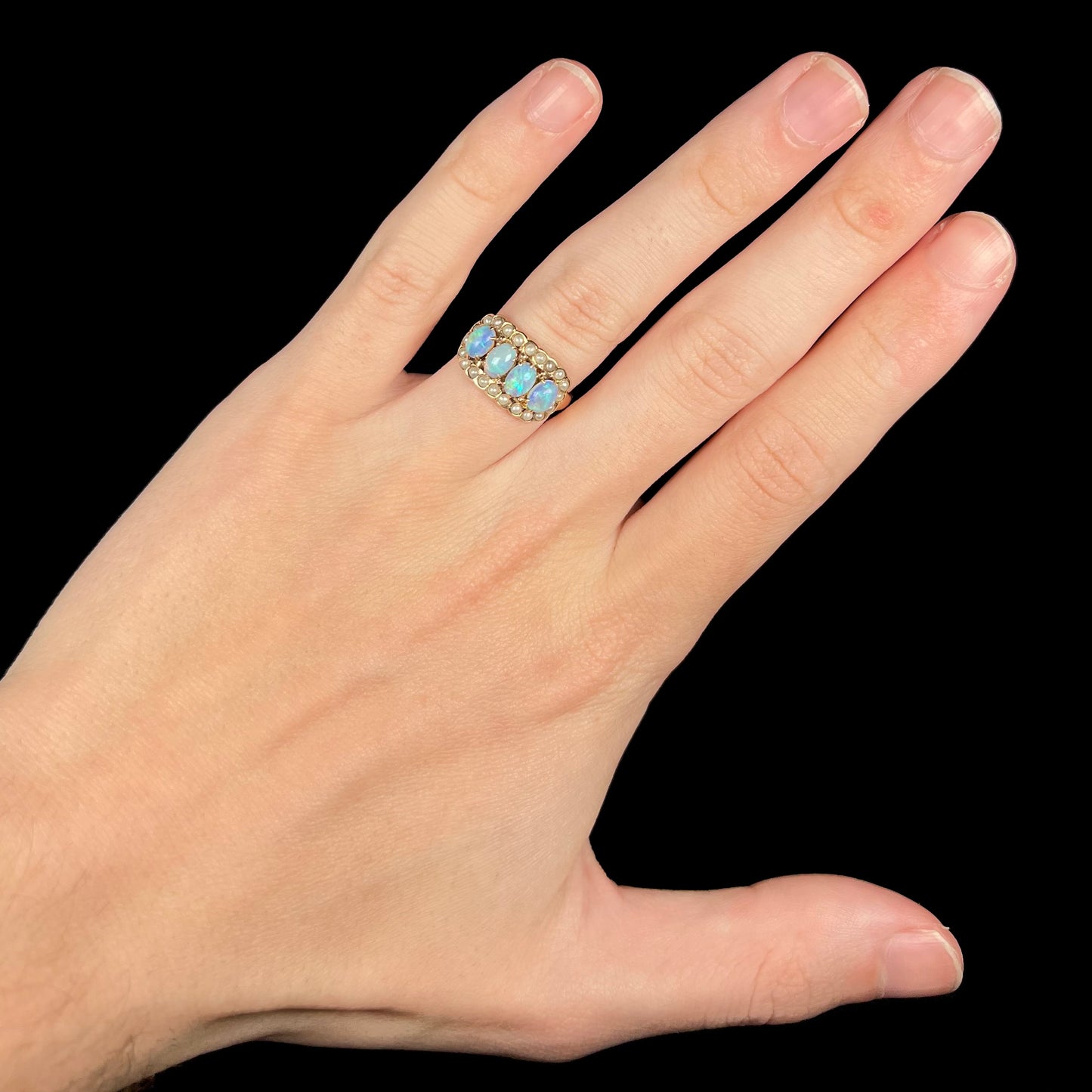 Hand wearing antique women's Victorian 9k gold opal and seed pearl ring under LED studio light