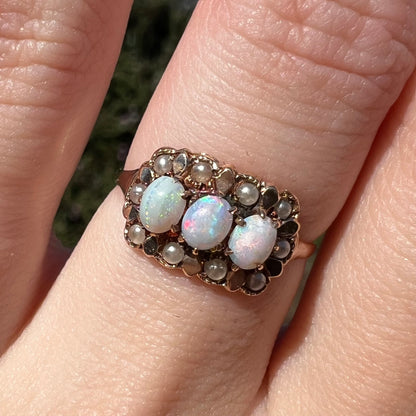 Macro view of women's Victorian three-stone opal and seed pearl halo ring in 9k gold, worn on finger and shown under natural sunlight