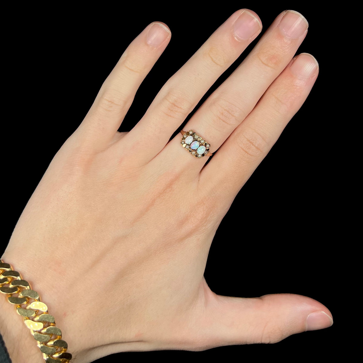 Hand wearing a Victorian era women's three-stone Australian opal and seed pearl halo ring in 9k gold under cool LED studio light
