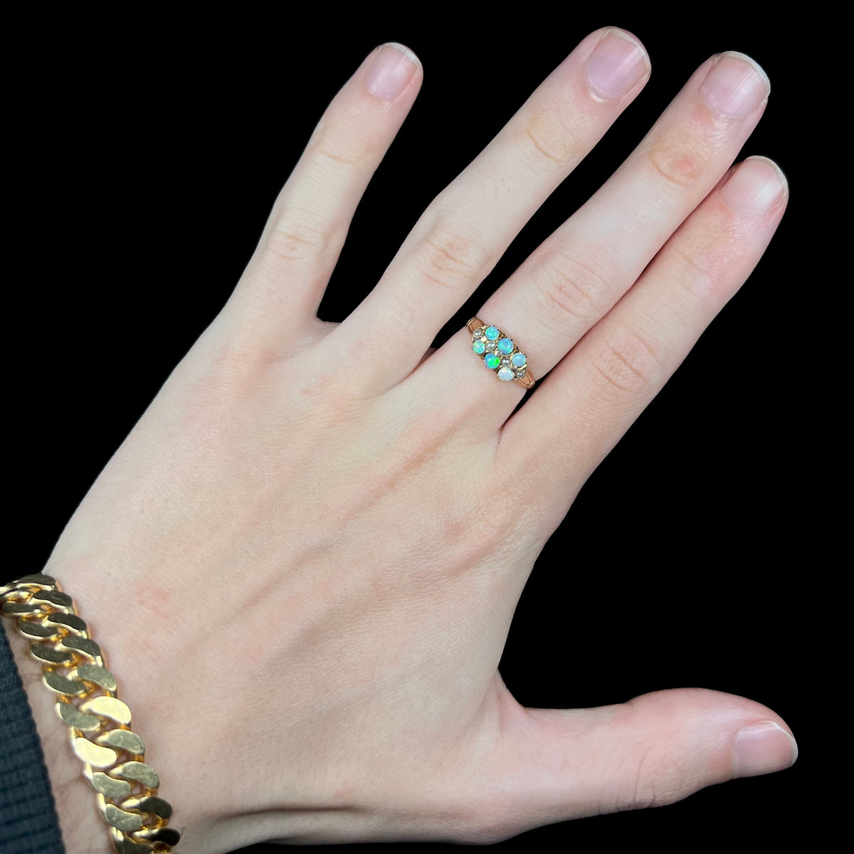 Hand wearing women's Victorian six-stone opal and pearl-accented ring on middle finger under cool LED studio lights