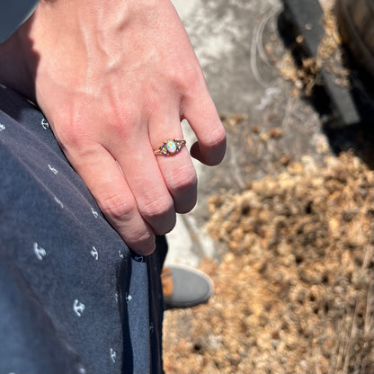 Person's hand resting on hip in natural light wearing women's dainty Victorian opal and seed pearl ring in 9k gold
