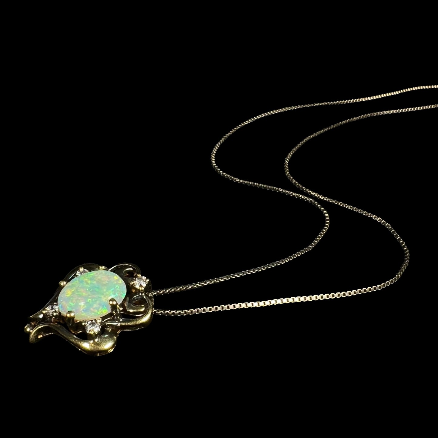 Angled view of a women's Victorian-style lab-created opal and cubic zirconia necklace laying on a black background, its silver chain trailing behind it.
