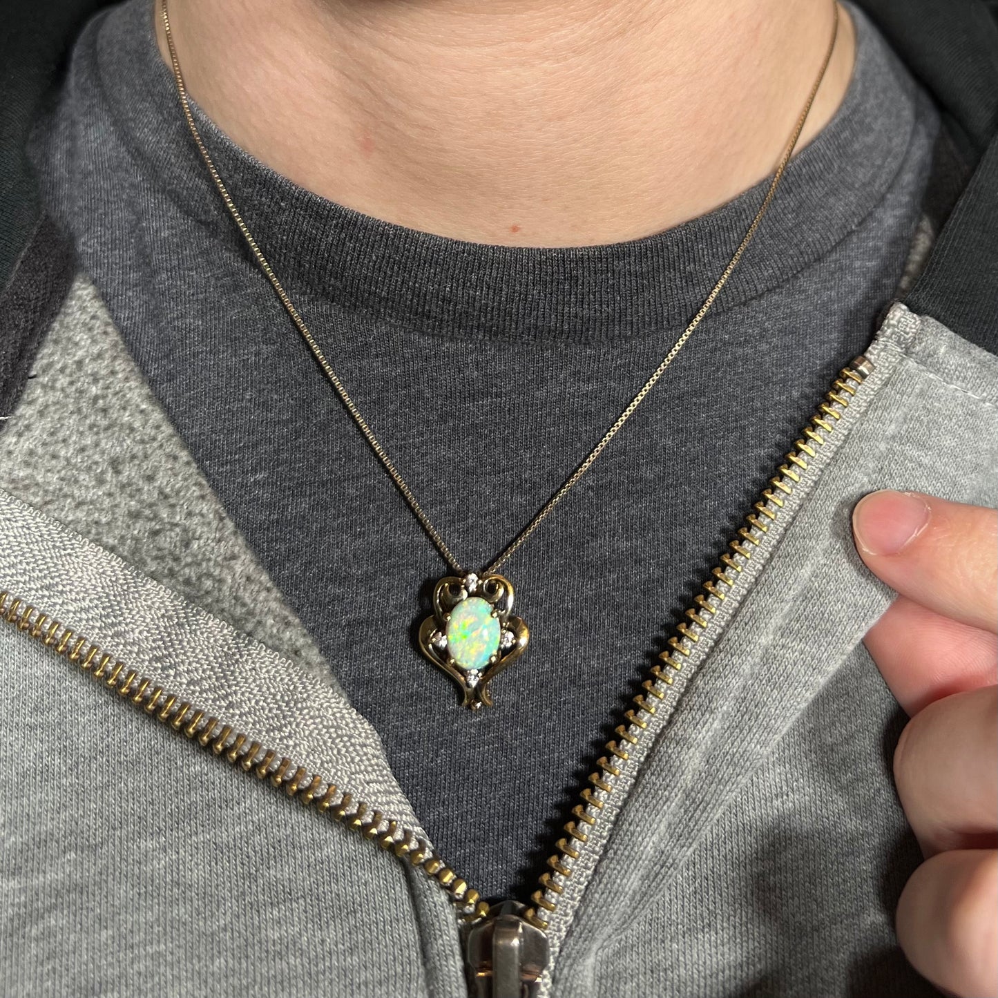 Close-up of person wearing a Victorian-style women's opal necklace around their neck against a dark shirt beneath a hoodie.