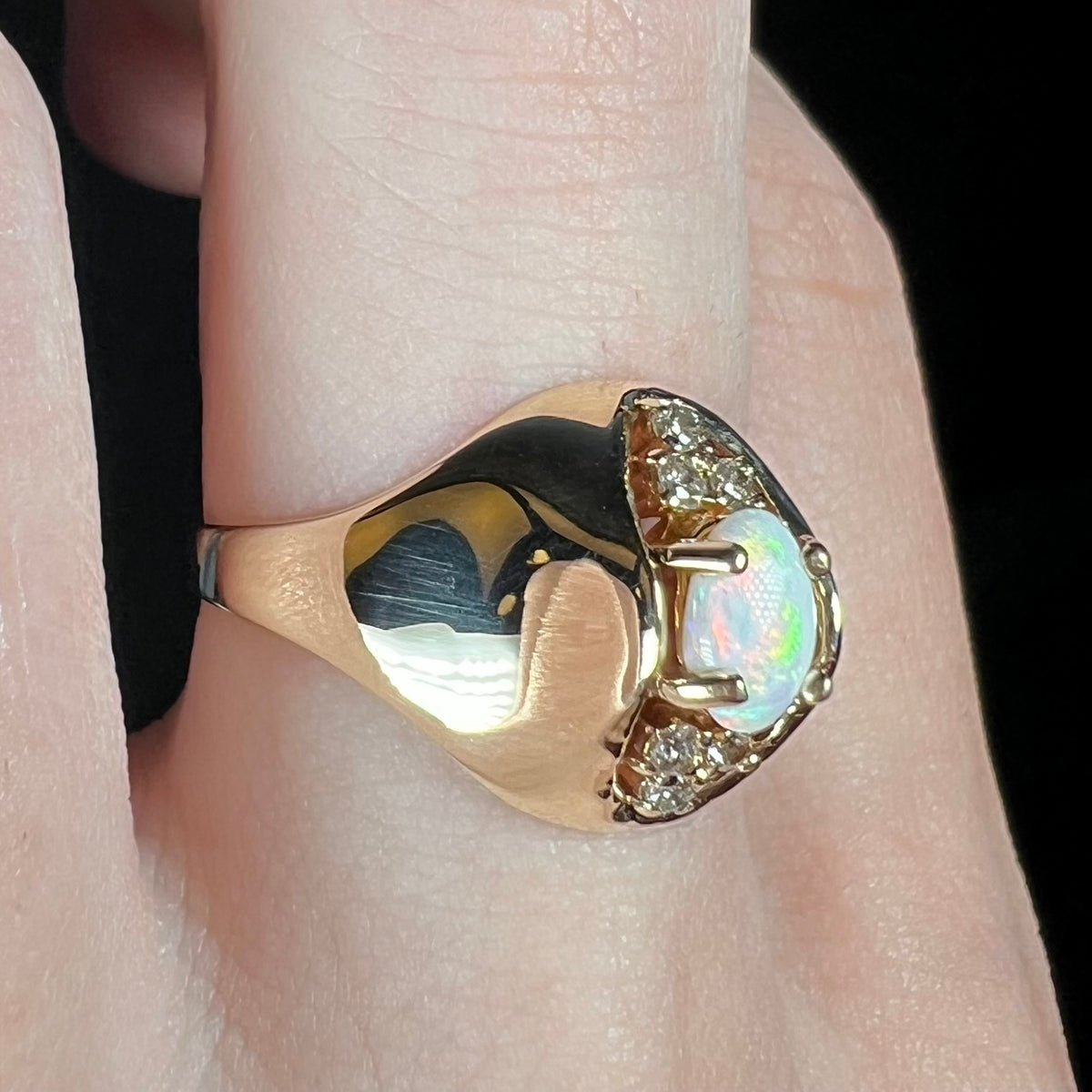 A vintage 1960s era women's opal and diamond ring with 14k gold domed design, worn on finger and viewed close-up from angle