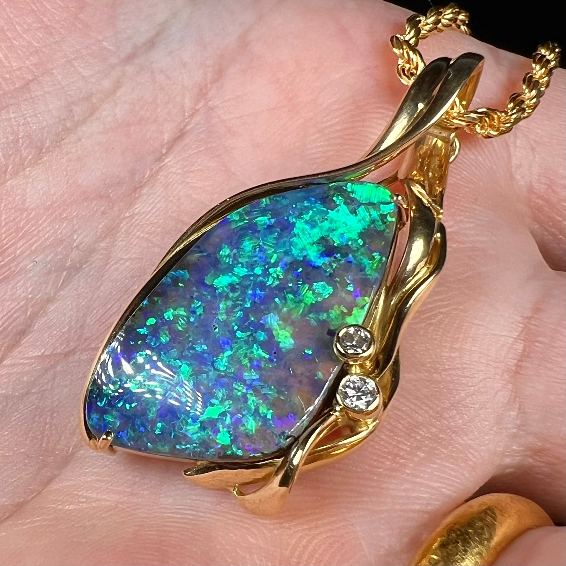 Angled close-up of women's vintage modernist style Australian boulder opal pendant in 18k gold, held in hand. The opal has green flashes of color.