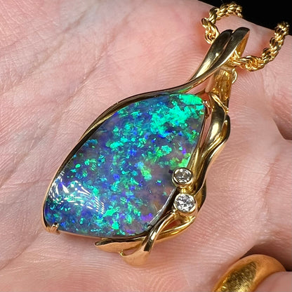 Angled close-up of women's vintage modernist style Australian boulder opal pendant in 18k gold, held in hand. The opal has green flashes of color.
