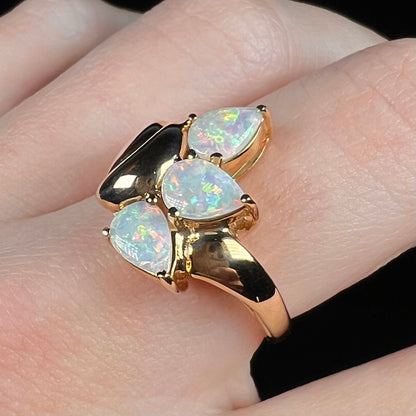 Angled close-up of a women's vintage, Modernist-style gold opal ring, worn on a finger under cool LED light.
