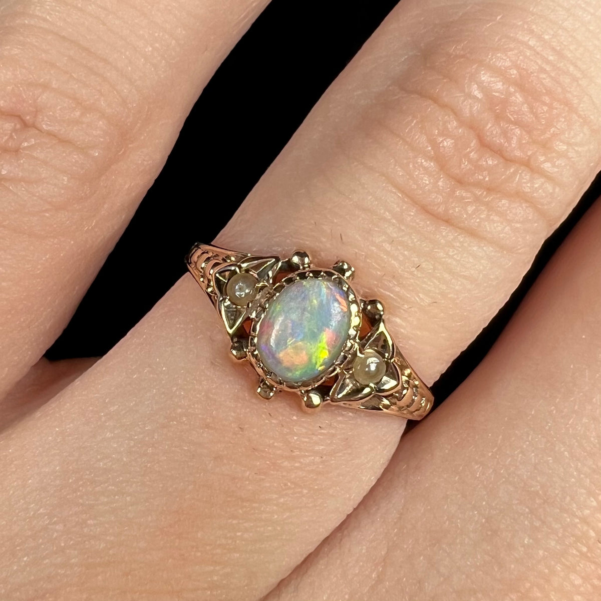 Close-up of women's antique White Cliffs, Australian opal and seed pearl ring, worn on finger
