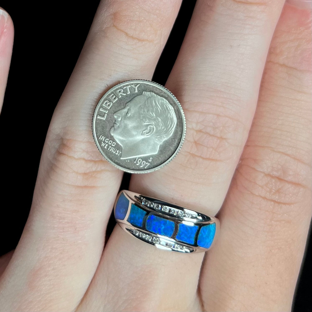 Close-up of hand wearing women's 14k white gold blue opal inlay ring with diamond accents; a US dime coin rests on the hand next to the ring