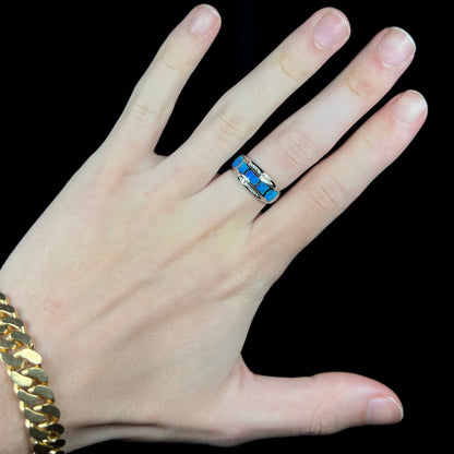 Hand wearing a women's 14k white gold Australian opal inlay ring with channel set diamond accents under cool LED studio light