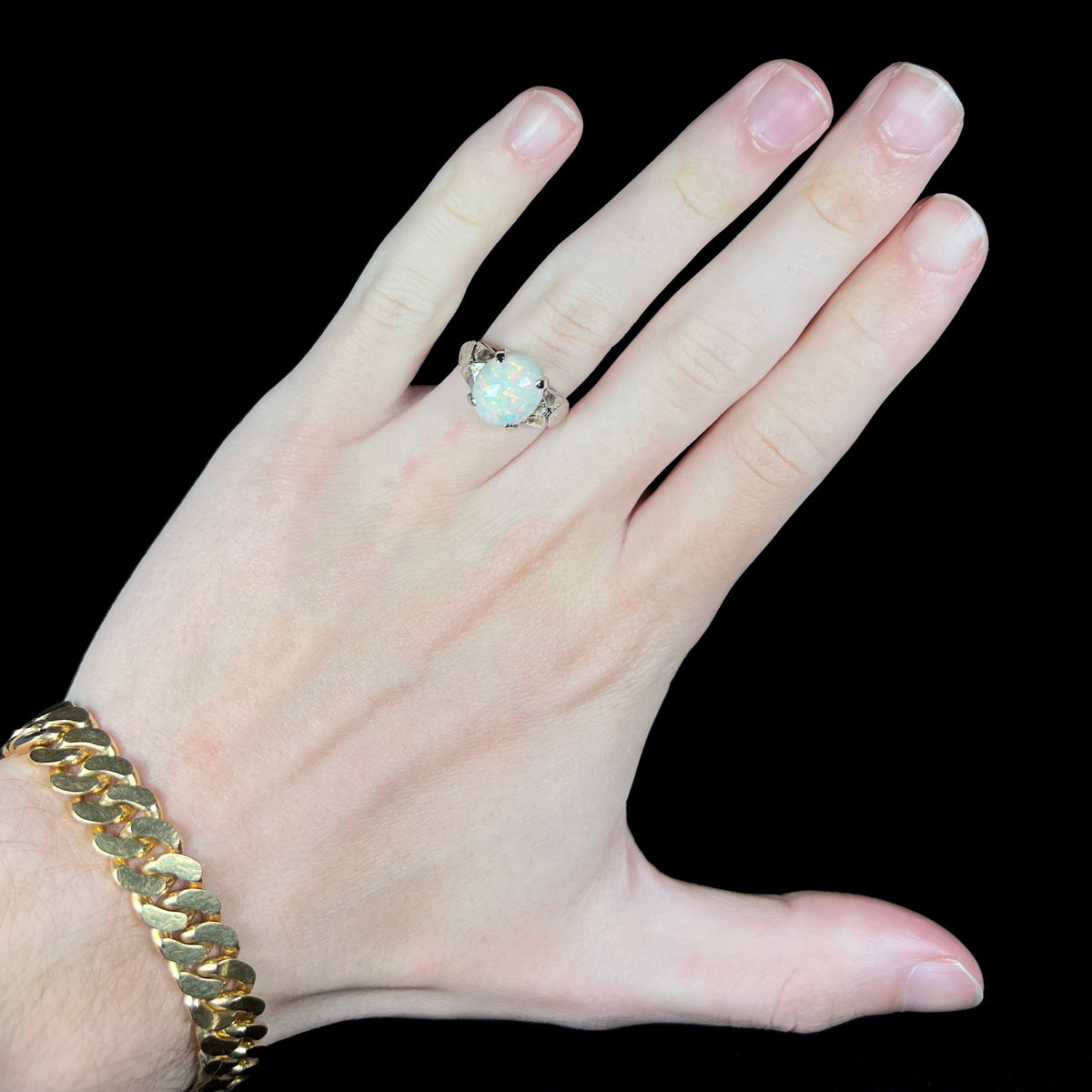 Hand wearing a women's 14k white gold Australian opal solitaire ring with textured shoulders under cool studio LED light