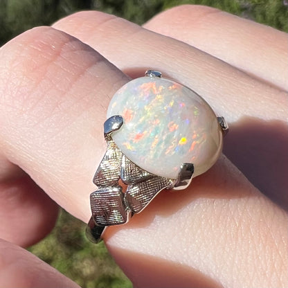 Angled close-up of a women's 14k white gold Australian opal solitaire ring, worn on a finger in natural light