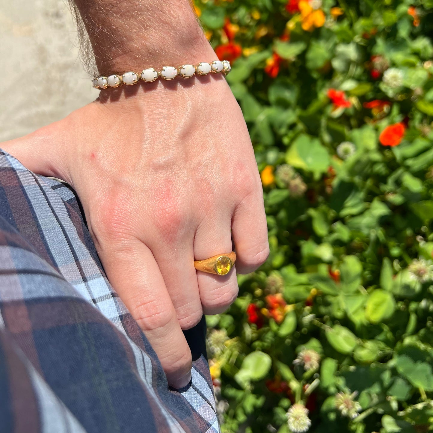 Hand resting on person's hip while wearing a gold ring and white opal tennis bracelet in sunlight.