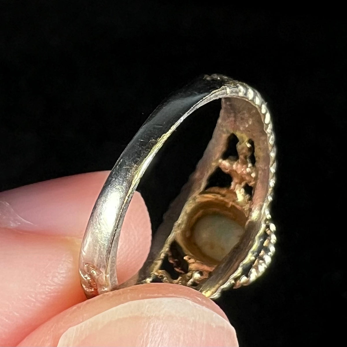 Bottom of estate base metal opal ring's shank, gold plating worn off to expose underlying base metal and sharp edges.