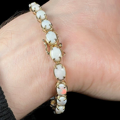 Underside of Australian white opal yellow gold tennis bracelet worn on a wrist shown close-up.  One opal shines with a red flash of color.