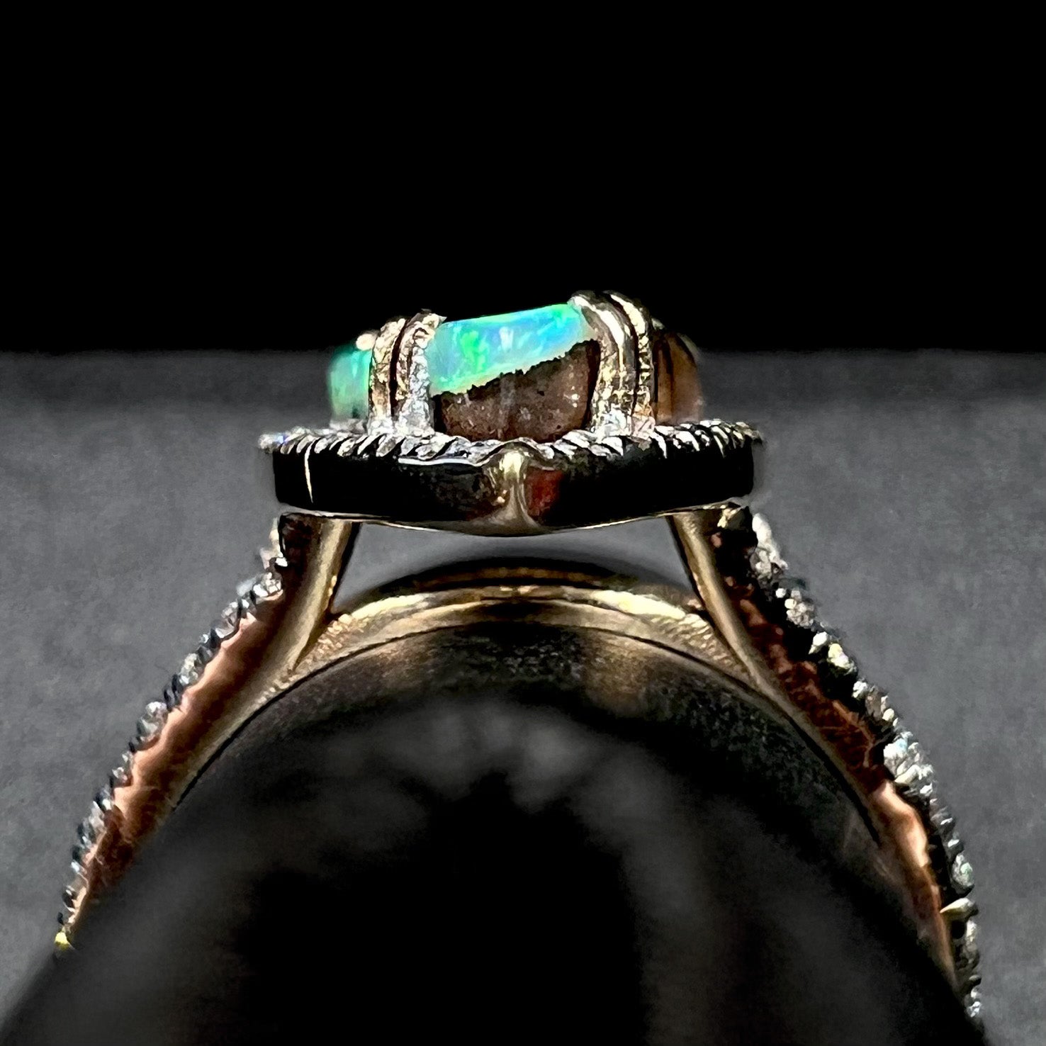 Side gallery profile view of a 14k yellow gold boulder opal and diamond engagement ring, shown on a ring display.