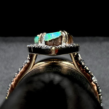 Side gallery profile view of a 14k yellow gold boulder opal and diamond engagement ring, shown on a ring display.