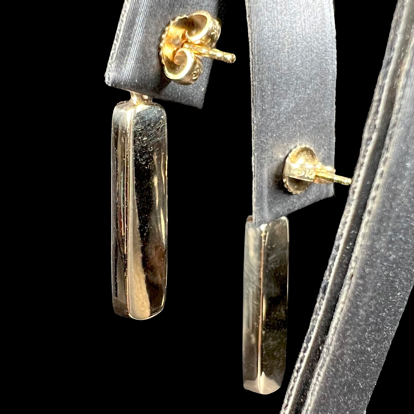 A pair of solid-backed yellow gold drop earrings, shown from the back against a black background.