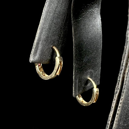Back view of a pair of yellow gold huggie hoop earrings, shown on an earring display against a black background.