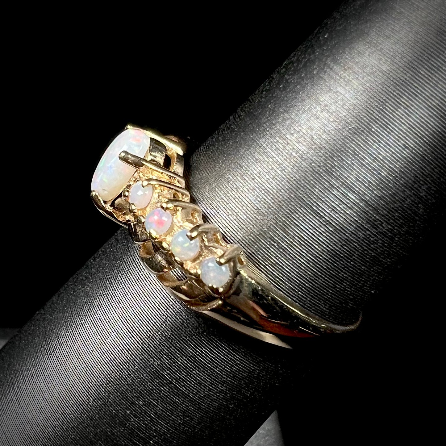 Side view of a yellow gold Australian white opal crisscross ring, shown on a ring display.