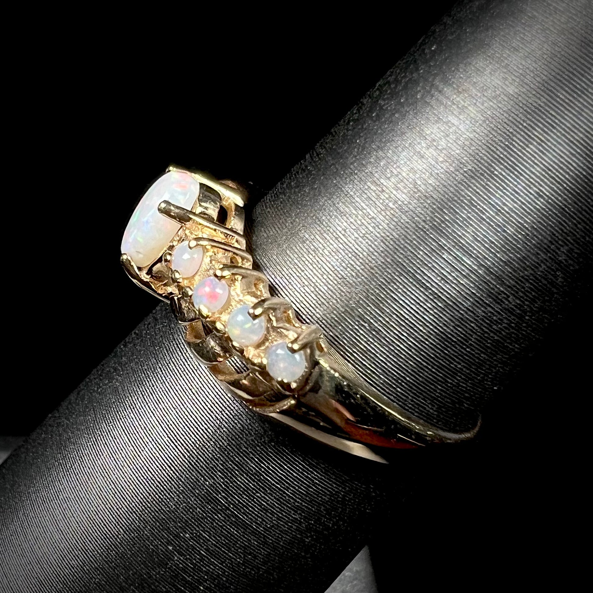 Side view of a yellow gold Australian white opal crisscross ring, shown on a ring display.
