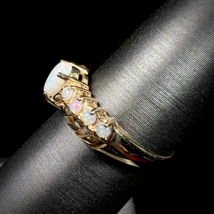 Side view of a yellow gold Australian white opal crisscross ring, shown on a ring display.
