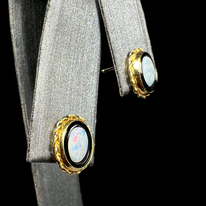 Yellow gold opal and onyx stud earrings shown from angle close-up on earring display against black background.
