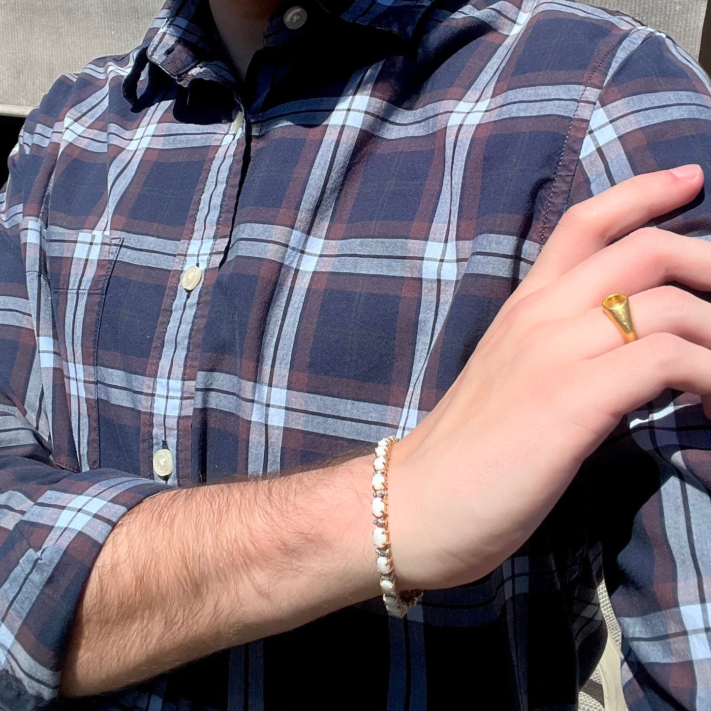 Person modeling a yellow gold opal and diamond tennis bracelet around wrist with 24k gold yellow sapphire ring on finger.  Their hand is resting on their opposing shoulder.