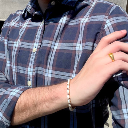 Person modeling a yellow gold opal and diamond tennis bracelet around wrist with 24k gold yellow sapphire ring on finger.  Their hand is resting on their opposing shoulder.