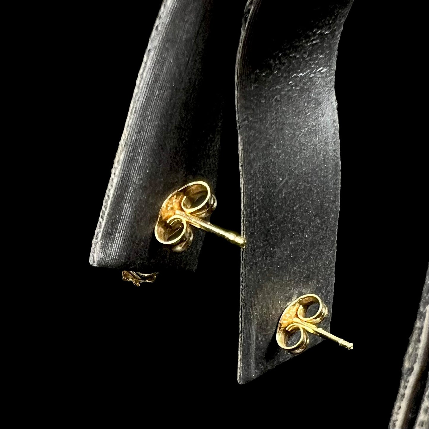 Back side of yellow gold push-back stud earrings on earring display.  Focus is on posts and butterfly backs.