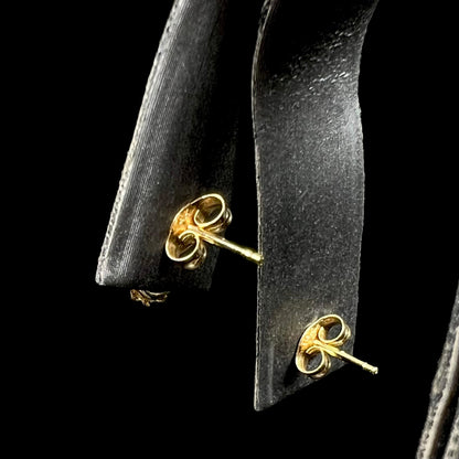 Back side of yellow gold push-back stud earrings on earring display.  Focus is on posts and butterfly backs.
