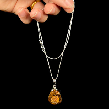 A Yowah nut boulder opal necklace in sterling silver, dangled from a hand by its chain.