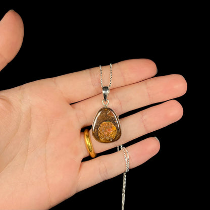 A Yowah nut boulder opal necklace in sterling silver, held in a hand shown against a black background.