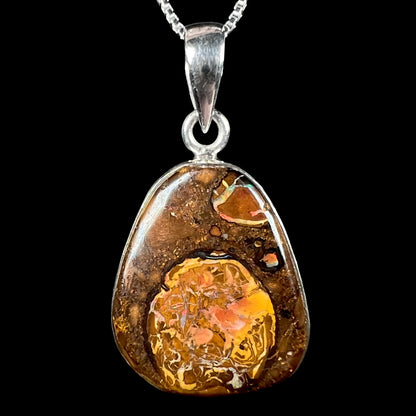 A Yowah nut boulder opal pendant in sterling silver shown close-up on a chain against a black background.