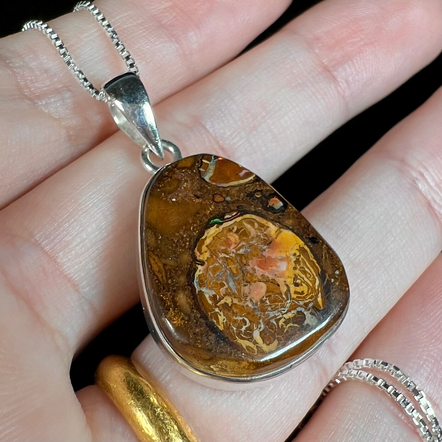 A Yowah nut boulder opal pendant in sterling silver, shown close-up from an angle in a hand.