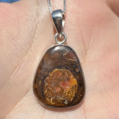 A Yowah nut boulder opal pendant in sterling silver shown close-up in the sunlight, held in a hand.