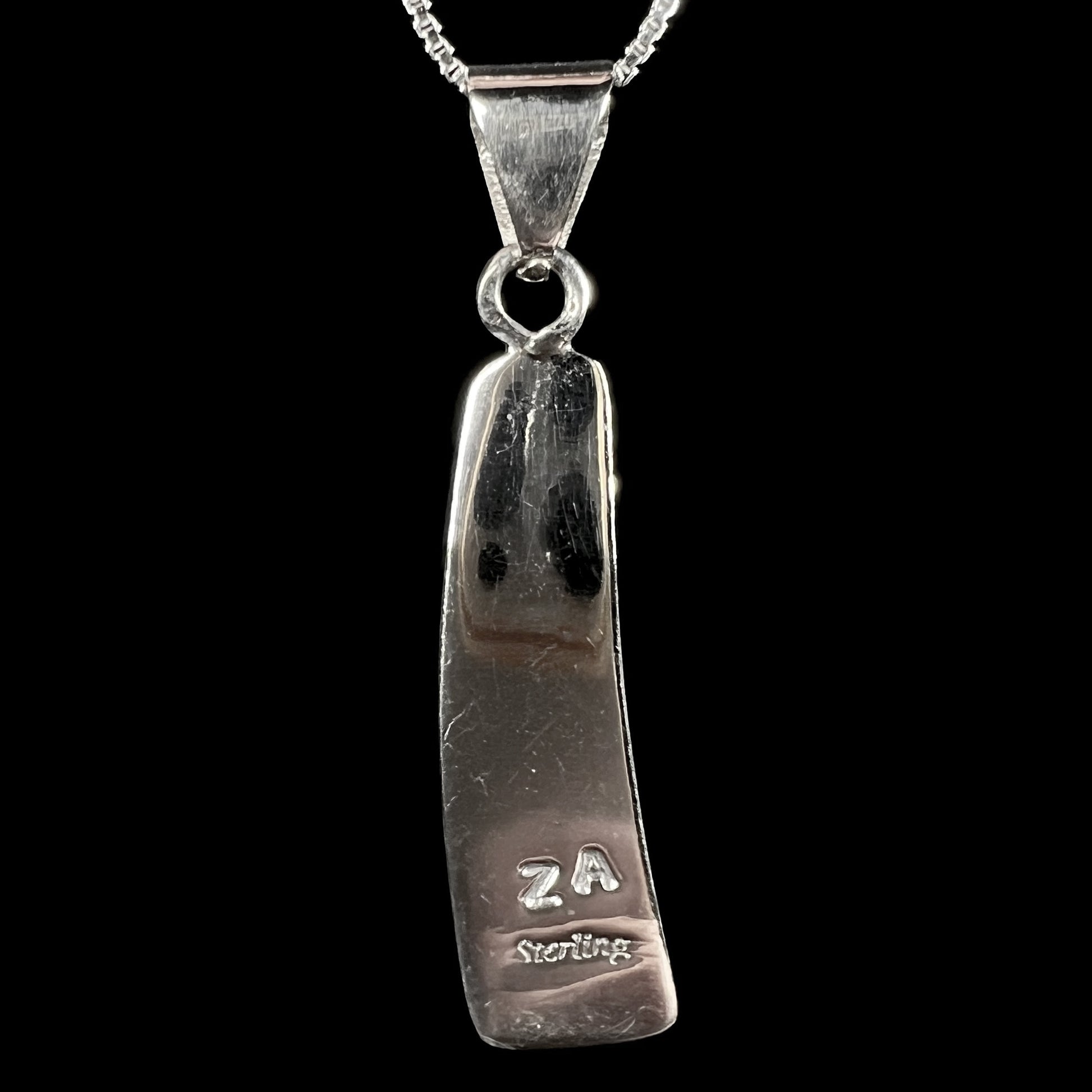 Back side of sterling silver pendant stamped "ZA STERLING", shown against black background.